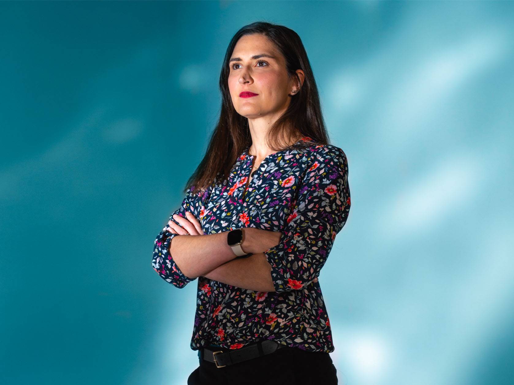 photo of woman standing with her arms crossed in front of light blue background